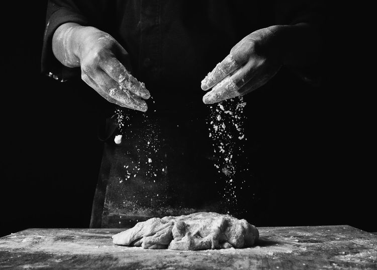 Midsection of chef preparing dough on table in darkroom