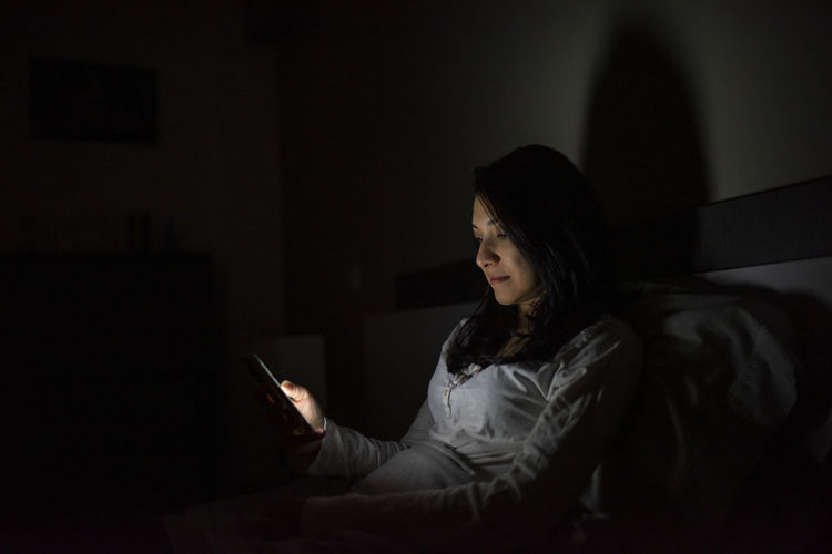 Latino woman using her cell phone before bed