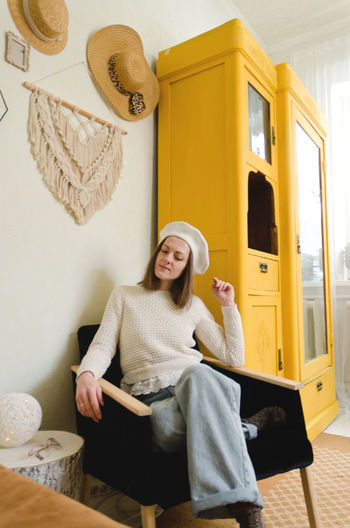 Young woman in beret sits in cozy home, room with music record in hands. vintage yellow cabinet.