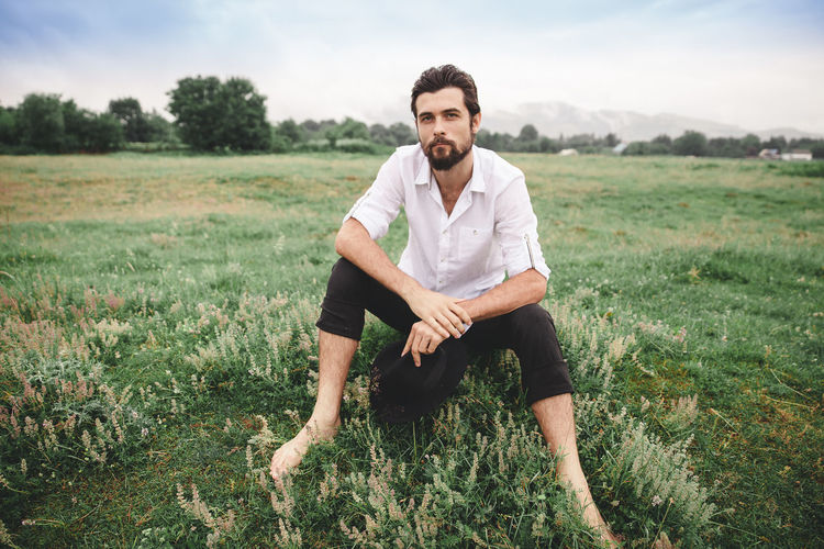 Full length portrait of young man sitting on grassy field