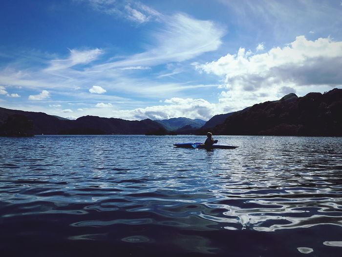Person kayaking in lake by mountains against sky