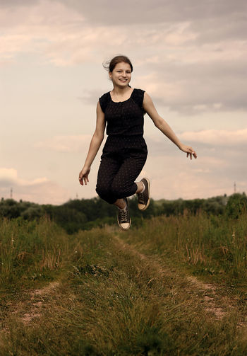 Full length of young woman jumping on field against sky