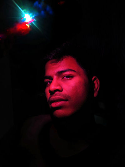 Portrait of young man with illuminated light against black background