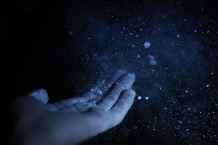 Cropped image of hand tossing dust against black background