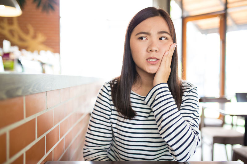 Young woman suffering from toothache while sitting in restaurant