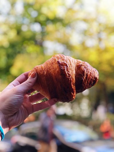 Close-up of woman hand holding croissant outdoors