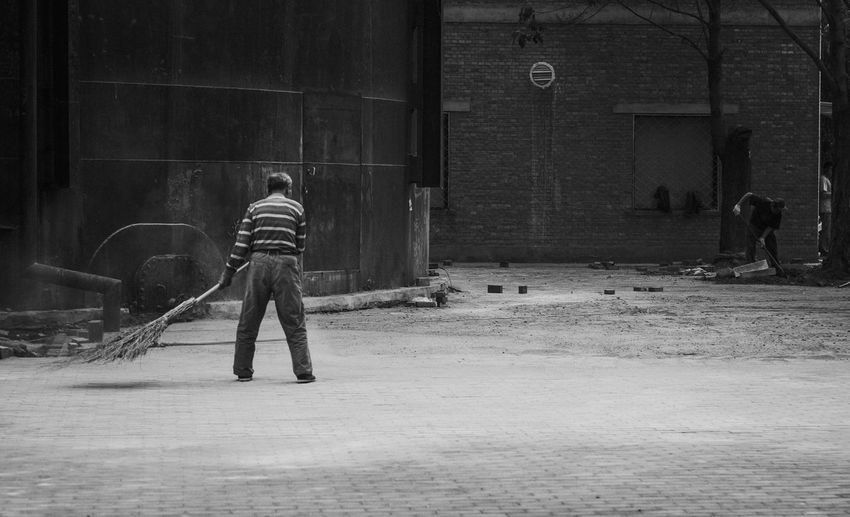 Full length rear view of sweeper cleaning street against building