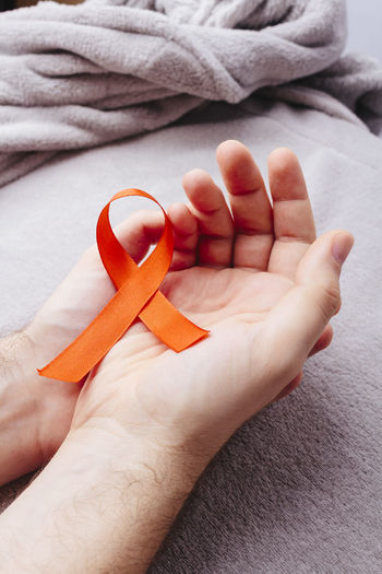 Cropped hands of man holding breast cancer awareness ribbon over bed