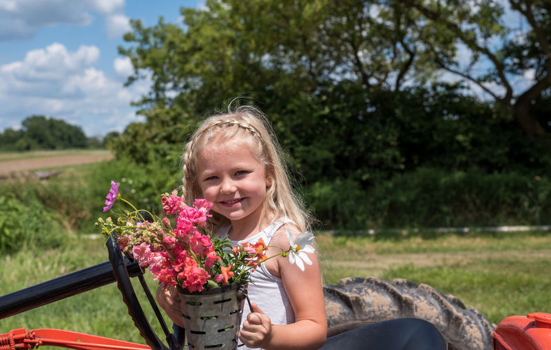 Portrait of cute girl holding flowers standing on field