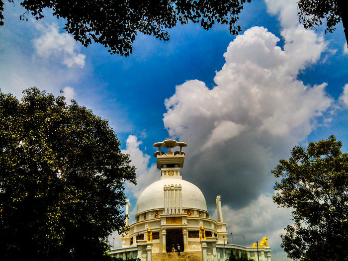 Shanti stupa at dhauligiri by trees against cloudy sky
