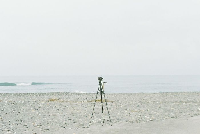 Camera on tripod at beach against clear sky