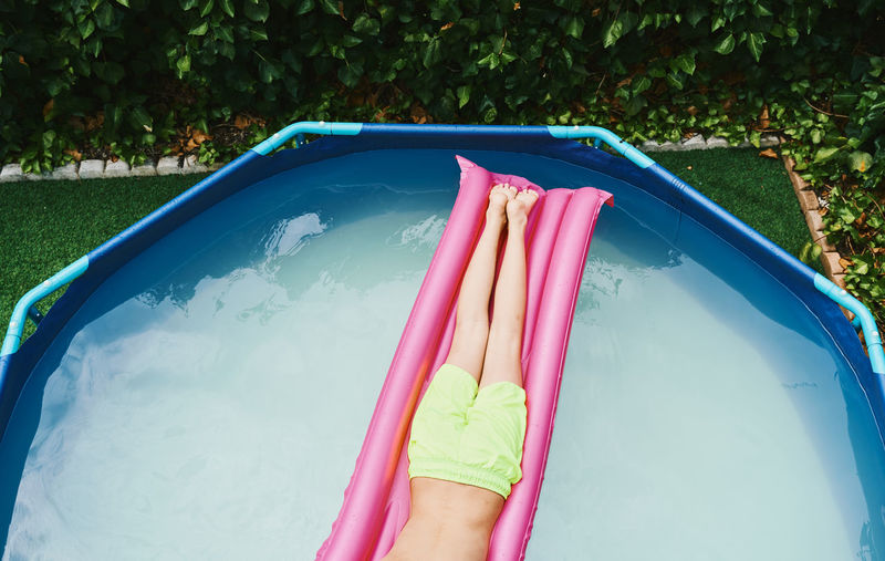 Cenital view of part of a boy lying on a pink float resting in a pool.
