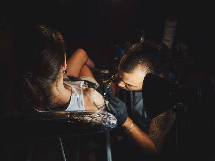 High angle view of artist making tattoo on woman hand