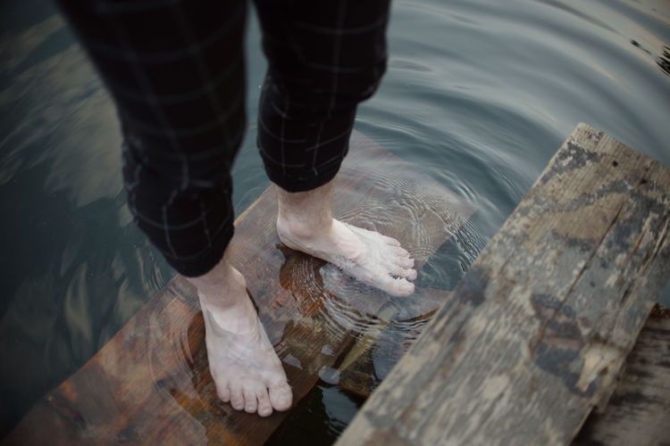 Low section of woman standing on wood by lake