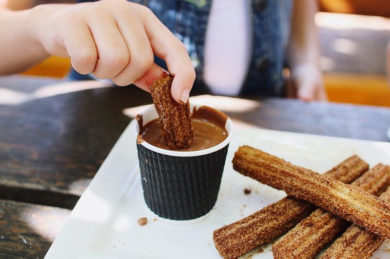 Midsection of woman dipping churro in chocolate at table