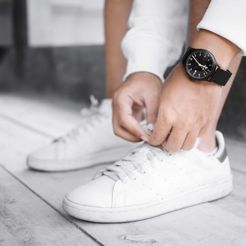 A man is tying his shoes and wearing a fancy watch