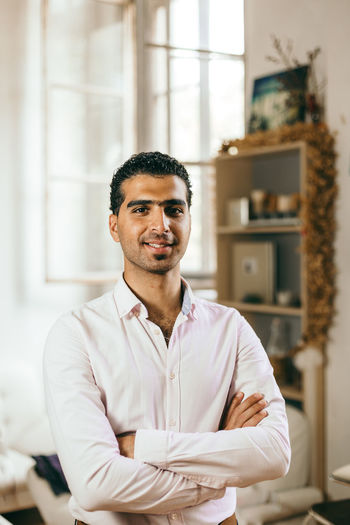 Portrait of smiling young man standing with arms crossed at home