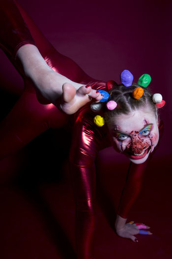 Portrait of woman with face paint wearing clown costume on colored background