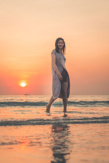Full length portrait of young woman on beach during sunset