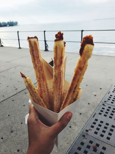 Cropped hand holding snacks against sea