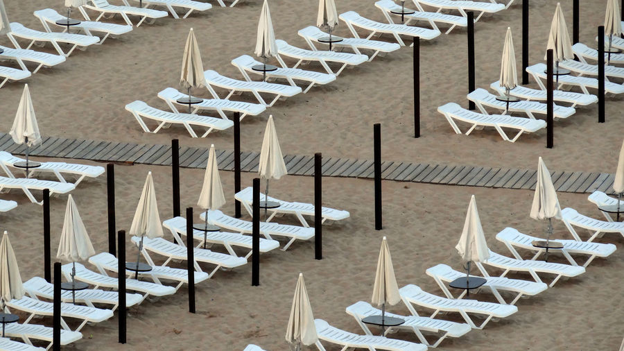High angle view of empty deck chairs and closed parasols at beach