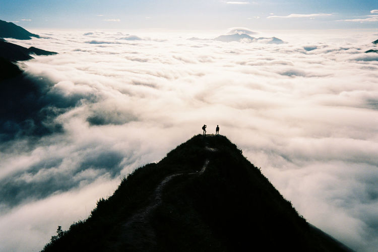 People standing on mountain against cloudscape