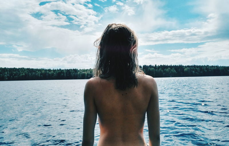 Rear view of shirtless woman by lake
