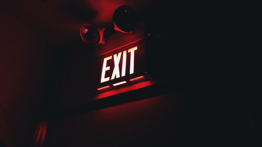 Low angle view of illuminated exit sign on wall in dark