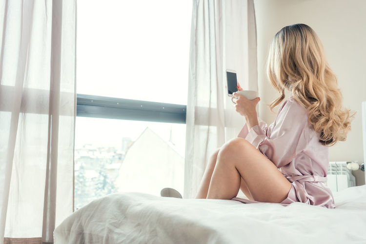 Midsection of woman using mobile phone while sitting on bed