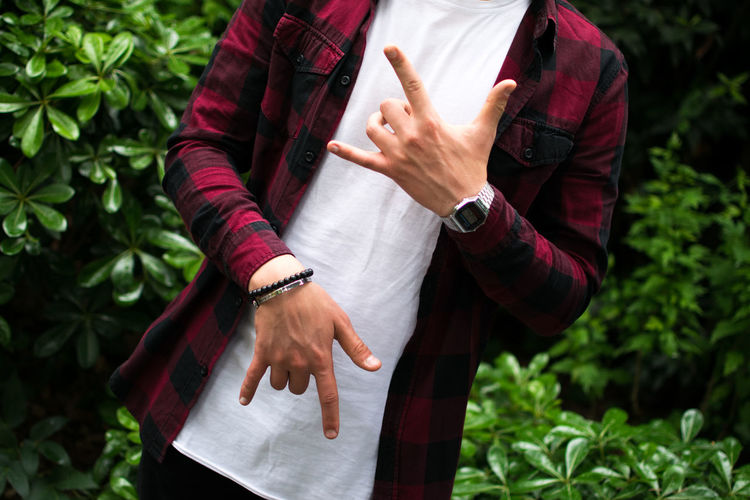 Midsection of man gesturing while standing against plants