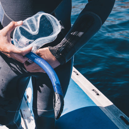 Cropped image of man holding snorkel while standing in boat