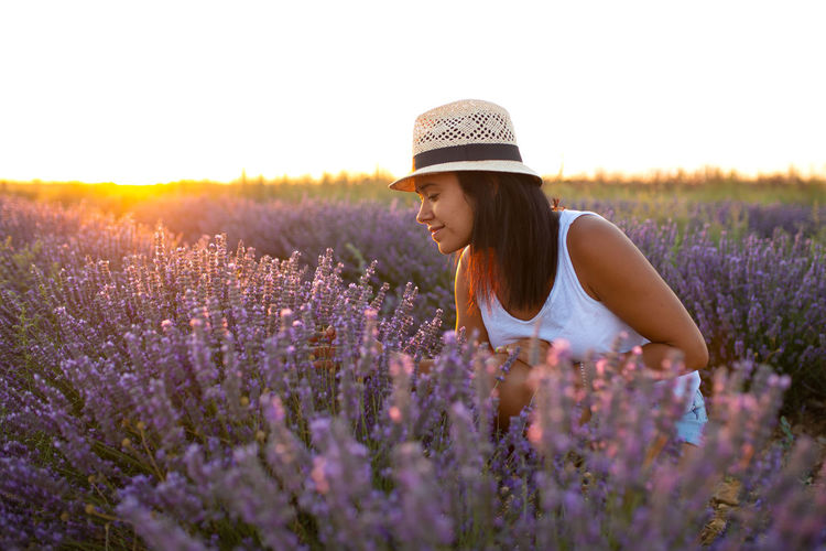 Young woman in hat enjoys nature in lavender flowers at sunset