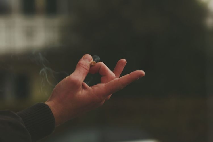 Close-up of cropped hand holding cigarette emitting smoke