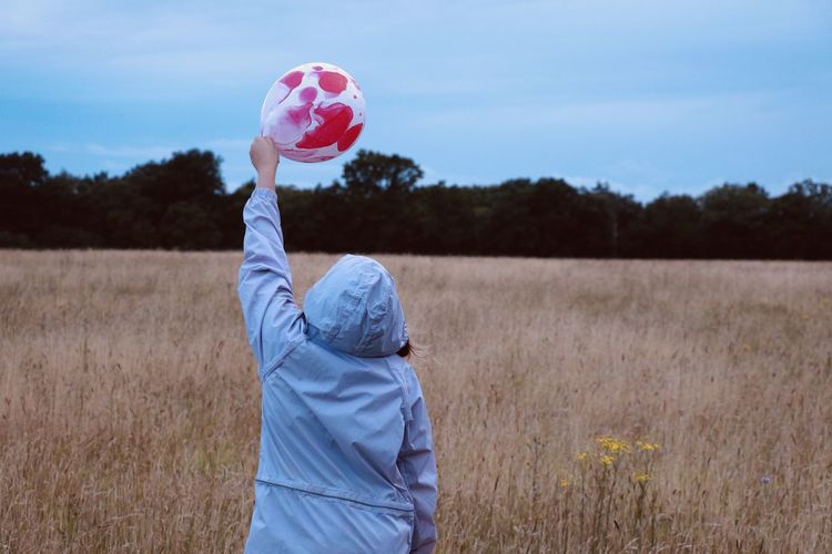 Rear view of girl holding balloons on field against sky