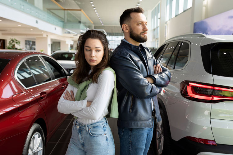 Thoughtful couple with arms crossed in car showroom