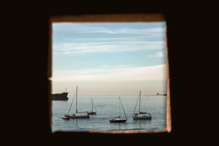 Sailboats sailing in sea against sky seen through window