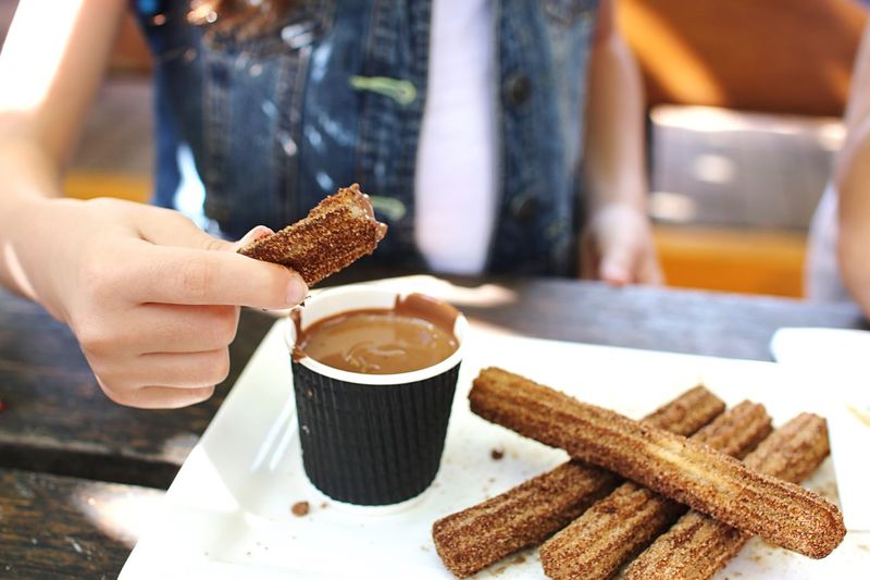 Midsection of woman dipping churro in chocolate at table