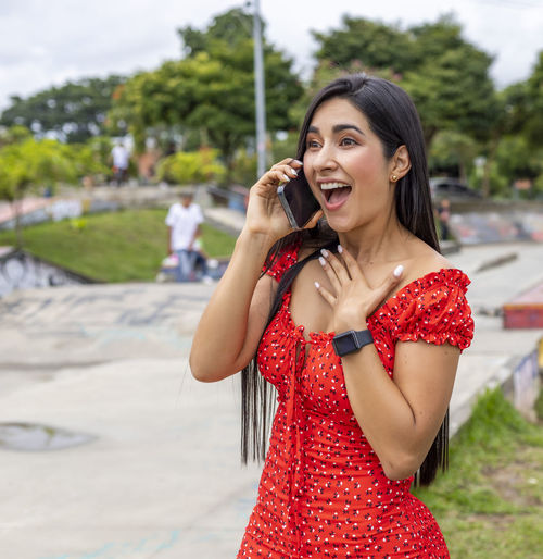 Happy young woman holding mobile phone while standing outdoors