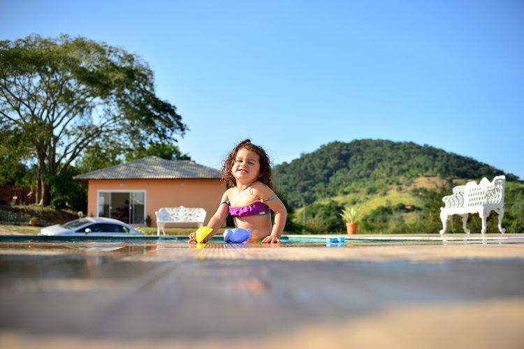 Portrait of cute girl in swimming pool against clear blue sky