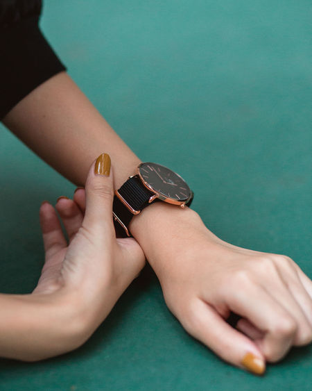 Cropped hands of woman wearing wristwatch on green table