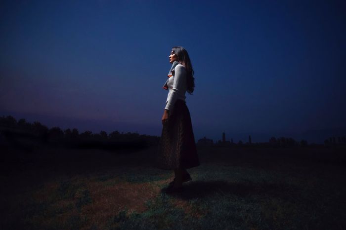 Side view of young woman standing on grassy field at night