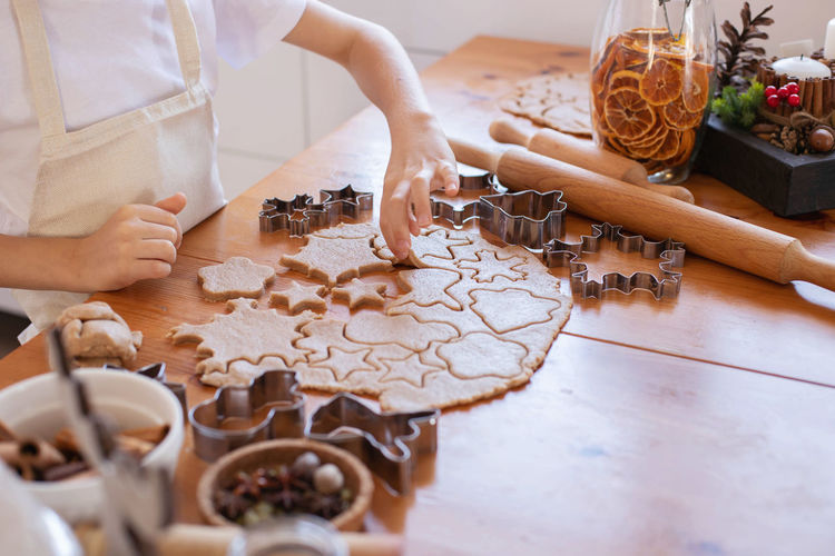Children with their mother cut out christmas gingerbread cookies on the table from rolled dough. 