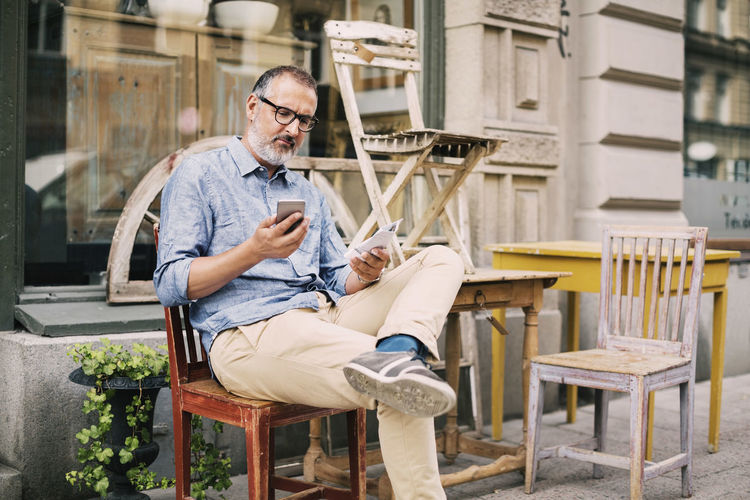 Man using mobile phone while sitting on chair outside antique shop