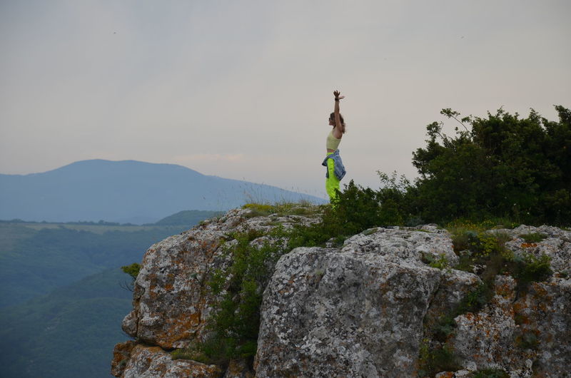 Man jumping on rock by mountain against sky