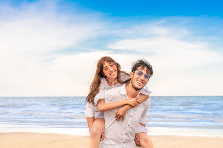 Portrait of couple enjoying on beach against sky