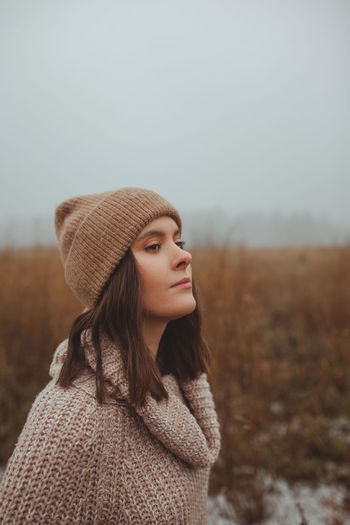 Portrait of beautiful young woman standing on land against sky during winter