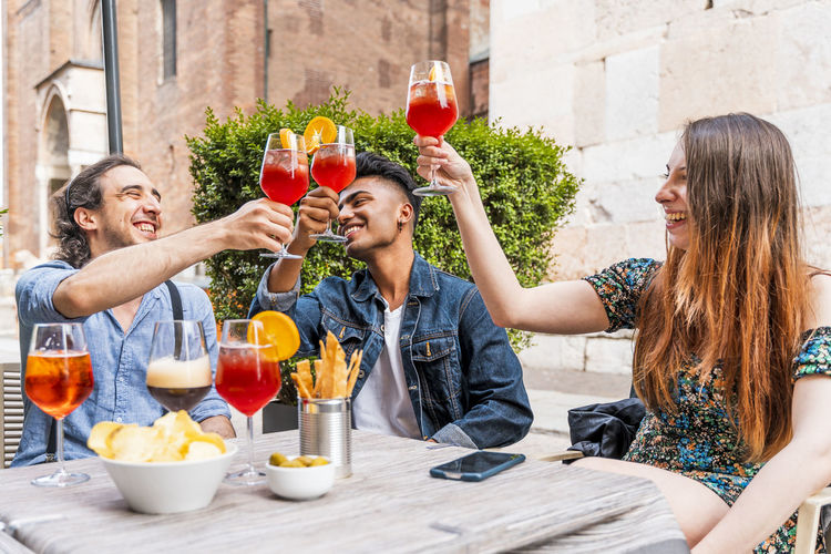 Smiling friends toasting drinks while sitting at cafe