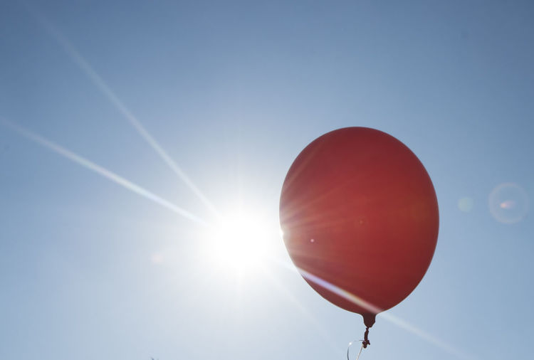 Red balloon and blue sky background with sun, symbol for joy and happiness