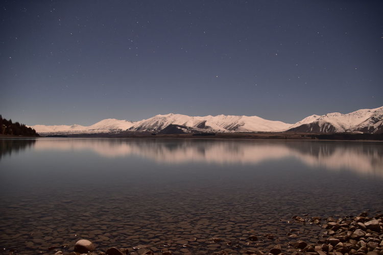 Scenic view of lake and snowcapped mountains against sky at night