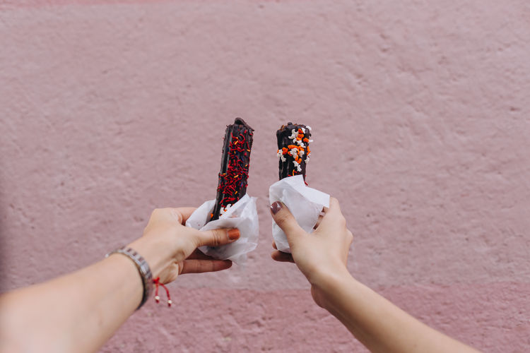 Two women holding churros with chocolate against a pink wall 